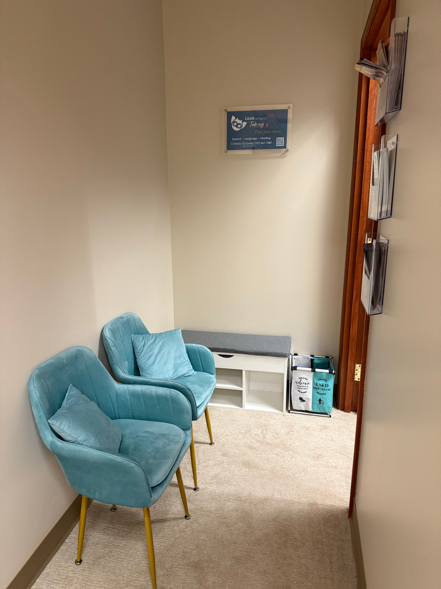 Waiting area with two teal velvet chairs, gray bench, and framed logo sign
