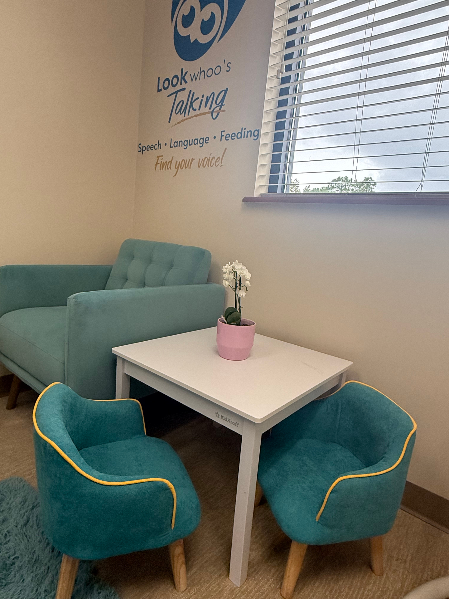 Waiting area with teal chairs, white table, and Look Whoo's Talking logo wall