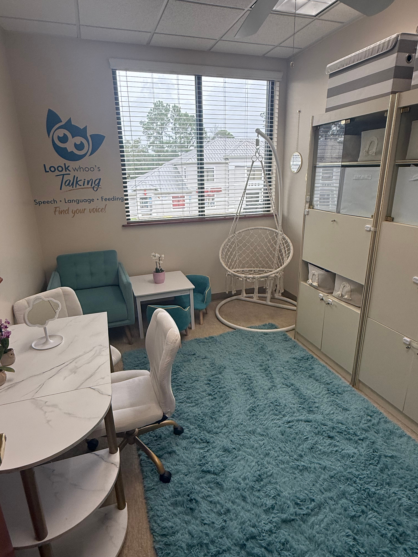 Therapy room with teal chairs, hanging chair, and Look Whoo's Talking logo wall